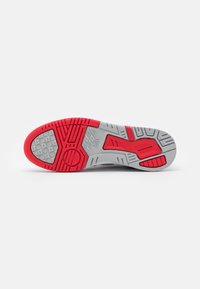 Semelle de chaussure avec motif d’adhérence en caoutchouc rouge et gris, présentant une bande de roulement texturée et le logo ASICS près du centre.