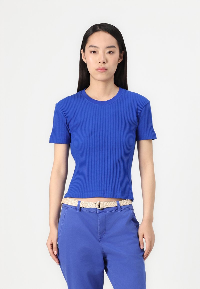 Niebieska, prążkowana bluzka z krótkim rękawem i okrągłym dekoltem, zestawiona z dopasowanymi niebieskimi spodniami oraz plecionym beżowym paskiem dla kontrastu.