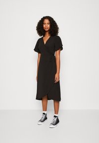Robe noire à manches courtes avec un lien à la taille, associée à des baskets montantes noires et des chaussettes blanches mi-mollets.