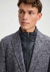 Blazer in un misto lana grigio-azzurro testurizzato, con una giacca interna trapuntata e con zip di colore scuro. Rever a lanciae tessuti a contrasto.