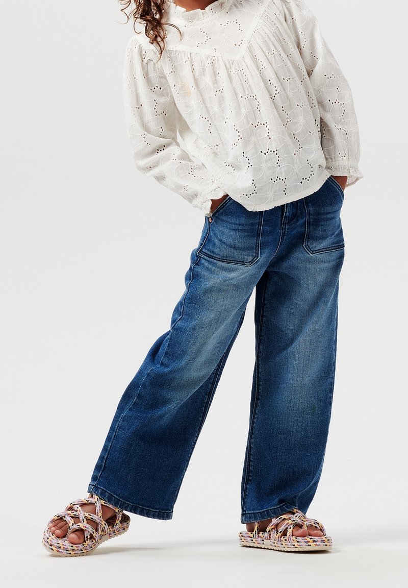 Light-weight white cotton blouse with eyelet details, paired with blue wide-leg denim jeans and multicolored woven sandals.