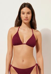Burgunderfärgad stickad bikiniöverdel med triangulära koppar och tunna remmar, med en texturerad finish. Matchande högmidjade bikiniunderdelar med snörningar.