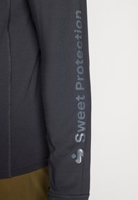 Zwart sportief langetermijnshirt met een strakke pasvorm, een gladde textuur en 'Sweet Protection' in reflecterend zilver langs de arm bedrukt.