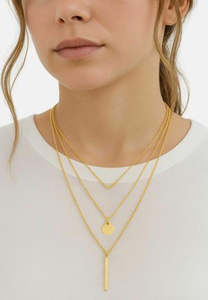 Collane d'oro a strati con catene intrecciate, dotate di un pendente circolare e un pendente rettangolare, indossate su una maglietta bianca.