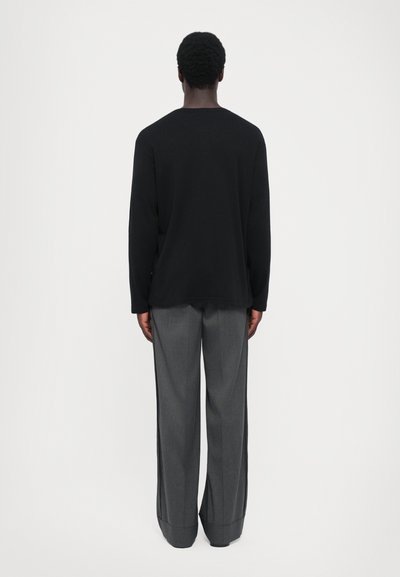 Čierna košeľa s dlhým rukávom so rovný strihom v kombinácii so šedými širokými nohavicami s jemnou textúrou a prehnutými manžetami.