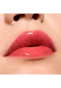 Glanzende lipkleur in een verloop van zachte roze en koraaltinten, waarbij de gladde textuur en volle vorm worden benadrukt tegen een lichte huidachtergrond.