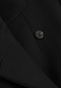 Schwarzer Wollblazer mit einem Reverskragen und einem auffälligen schwarzen Knopf an der Verschlussstelle, mit feiner Textur und maßgeschneiderten Designdetails.