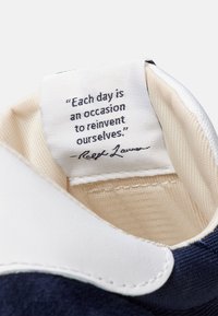 Vitt och blått sneakers innertill med en tygetikett som har ett citat av Ralph Lauren i svart text på en beige bakgrund.