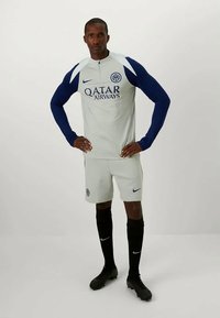 Completo da allenamento di calcio composto da una maglietta grigia chiara con maniche blu navy, logo del club e testo "Qatar Airways", abbinato a pantaloni corti coordinati e calze nere.