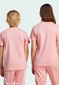 Pink cotton t-shirts with short sleeves, featured on two figures from the back, paired with matching pink pants, smooth texture.