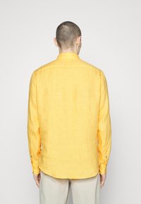 Žlutá lněná košile s dlouhým rukávem, kulatým lemem a zapínáním na knoflíky, vyrobená z texturované látky bez vzorů nebo ozdob.