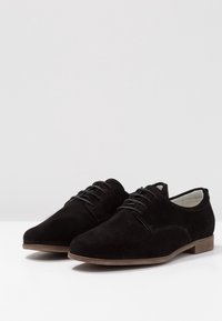 Scarpe in suede nere con lacci, punta arrotondata, cuciture minime e suola marrone chiaro. Fodera interna liscia e design semplice.