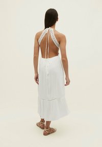 Robe blanche sans manches avec un design en crochet au niveau du col, un dos ouvert et un ourlet à volants. Tissu léger avec une coupe décontractée.