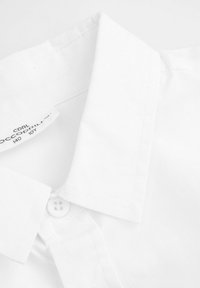 Biała koszula z kołnierzykiem wykonana z tkaniny bawełnianej, z zapięciem na guziki i teksturowaną powierzchnią z widocznym detalem szwów.