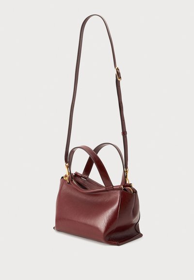 Sac à main en cuir rouge foncé avec bandoulière longue réglable et deux poignées courtes, présenté sur un fond clair uni.