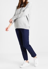 Ljusgrått stickat tröja med lös passform, sidoflikar, i kombination med marinblå byxor och vita sneakers. Enkelt design utan synliga mönster.