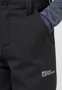 Mustad mustad püksid sileda tekstuuriga, küljetasku ja reie peal logo sildiga. Vöökoht on nupuga kinni.
