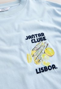 Chemise bleu clair avec texte brodé « Jantar Clube Lisboa » et illustration de trois poissons et tranches de citron.
