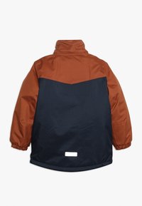 Giacca impermeabile con una parte superiore marrone e una parte inferiore blu navy, dotata di polsini elastici e un'etichetta riflettente sul retro.