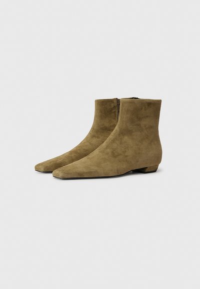 Botas de tobillo de ante marrón con punta afilada, tacón bajo y cremallera lateral. Textura suave y diseño minimalista.