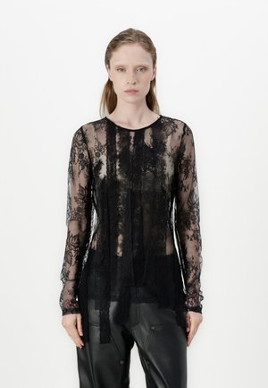 Black lace long-sleeve top featuring a floral pattern, sheer texture, round neckline, and layered design, paired with black trousers.