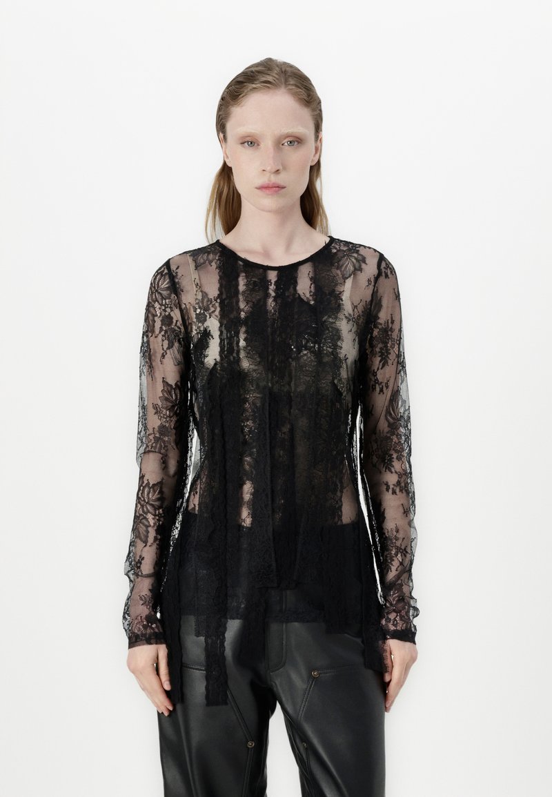 Black lace long-sleeve top featuring a floral pattern, sheer texture, round neckline, and layered design, paired with black trousers.