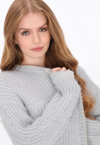 Helles graues Strickpullover mit strukturiertem Gewebe, ein Rundhalsausschnitt und feine goldene Fadenakzente entlang des Saums.