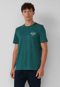 Teal T-shirt met korte mouwen van zacht materiaal, met een ronde hals en een kleine witte afbeelding op het linkerbovenborstgebied.
