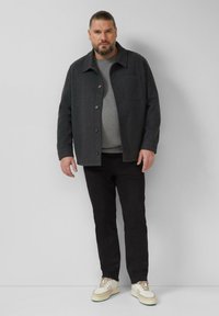 Szara kurtka z tkaniny z kołnierzem i zapięciem na guziki, zestawiona z szarym swetrem, czarnymi dżinsami i białymi tenisówkami. Prosta konstrukcja i faktury.