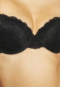 Black lace strapless bra with floral pattern, scalloped edges, molded cups, and a smooth texture.