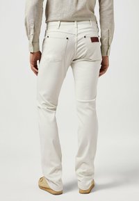 Jeans in denim bianco con vestibilità slim, dotati di tasche posteriori con cuciture a contrasto e una toppa in pelle marrone sulla vita.