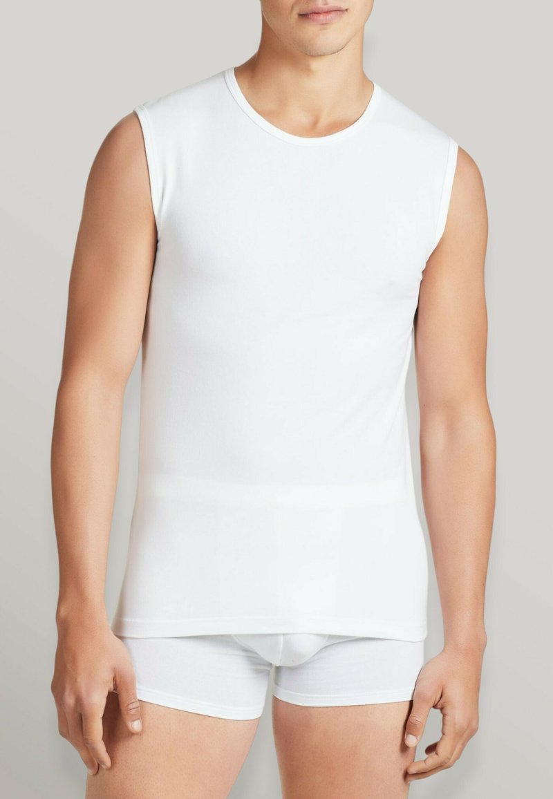 Maglietta senza maniche in cotone bianco con colletto rotondo, abbinata a pantaloni corti bianchi aderenti. Texture liscia, design minimalista, senza motivi visibili.