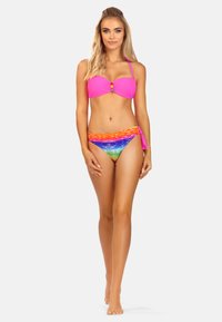 Różowy top bikini z przekręconym przodem i zdobnymi koralikami, połączony z kolorowymi, paskowanymi majtkami bikini w odcieniach pomarańczowego, niebieskiego i zielonego.