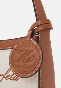 Étiquette en cuir marron embossée "RL" attachée à un sac en cuir couleur fauve et tissu beige avec des détails cousus.