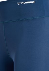 Granatowe legginsy sportowe wykonane z gładkiego, elastycznego materiału, z logo na pasie i płaskimi szwami dla większego komfortu.