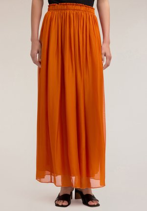 Lange, vloeiende oranje rok van lichtgewicht, doorschijnende stof met een elastische tailleband. Gecombineerd met zwarte sandalen met hakken.