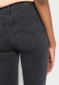 Jeans de mezclilla negros con una forma ajustada, que cuentan con un diseño de bolsillo trasero, etiqueta de marca y detalles de costura sutiles.