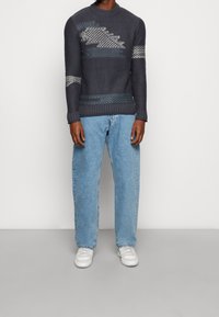 Merivoimien neulepaita, jossa on teksturoitu kuvio ja vaaleanharmaat yksityiskohdat, yhdistetty vaaleansinisiin, väljämallinen farkkuihin ja valkoisiin tennareihin.