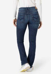 Donkerblauwe jeans met een getailleerd ontwerp, met twee achterzakken in een chevronpatroon en een leren logo patch op de tailleband.