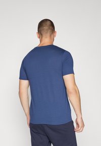 Marinblå t-shirt med kort ärm och rund halsringning. Slätt tyg och en figursydd design som visar minimala sömmar vid axlarna och sidorna.