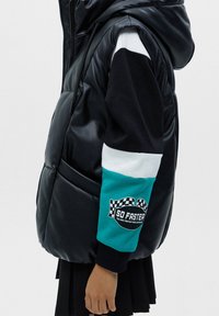 Veste noire matelassée à capuche avec une finition brillante, dotée de manches color-block en noir, blanc et sarcelle avec un détail logo à carreaux.