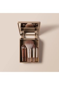 Kompakt beige etui med fem makeupbørster i ulike størrelser og et speil inni, arrangert på en lys beige bakgrunn.