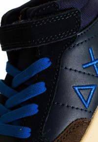 Sneaker alta con lacci blu, tomaia in pelle nera e suede, design multi-tonale, con dettagli di cucitura geometrica blu.