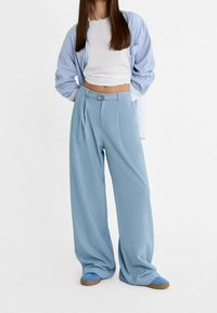 Lichtblauwe wijde broek met een riemdetail, plooien en een gladde textuur, gecombineerd met een witte cropped top en een gestreepte overhemden.