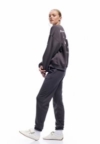 Mørkegrå sweatshirt med grafisk print på ryggen, parret med matchende sweatpants og hvide sneakers. Blødt stof med afslappet pasform og ribbede manchetter.