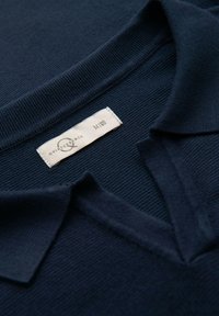 Marinblå pikétröja med korta ärmar och texturerad stickning; har en V-formad krage. Etiketten visar storlek M och varumärket.