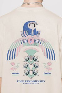Tricou de culoare crem, cu un design grafic mare al unei vulturi, înconjurat de simboluri antice în nuanțe de albastru, roz și verde. Textul spune "IMENSITATEA TIMPULUI".