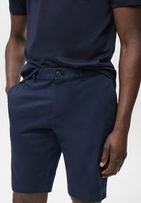 Marinblå shorts i lätt tyg, med knappstängning, sidofickor och rak skärning. Lämpliga för avslappnad klädsel.