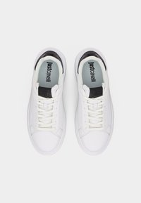 Ζευγάρι λευκά αθλητικά παπούτσια με κορδόνια, με μαύρες λεπτομέρειες στη γλώσσα και τη φτέρνα, απόψη από πάνω, με λογότυπο Just Cavalli στο εσωτερικό.