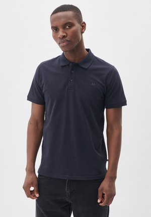 Tumedate tähniline polo-särk, puuvillane materjal, lühikesed varrukad, kolme nööbiga plisseering, rinnal logo, kantud tumedate teksadega.